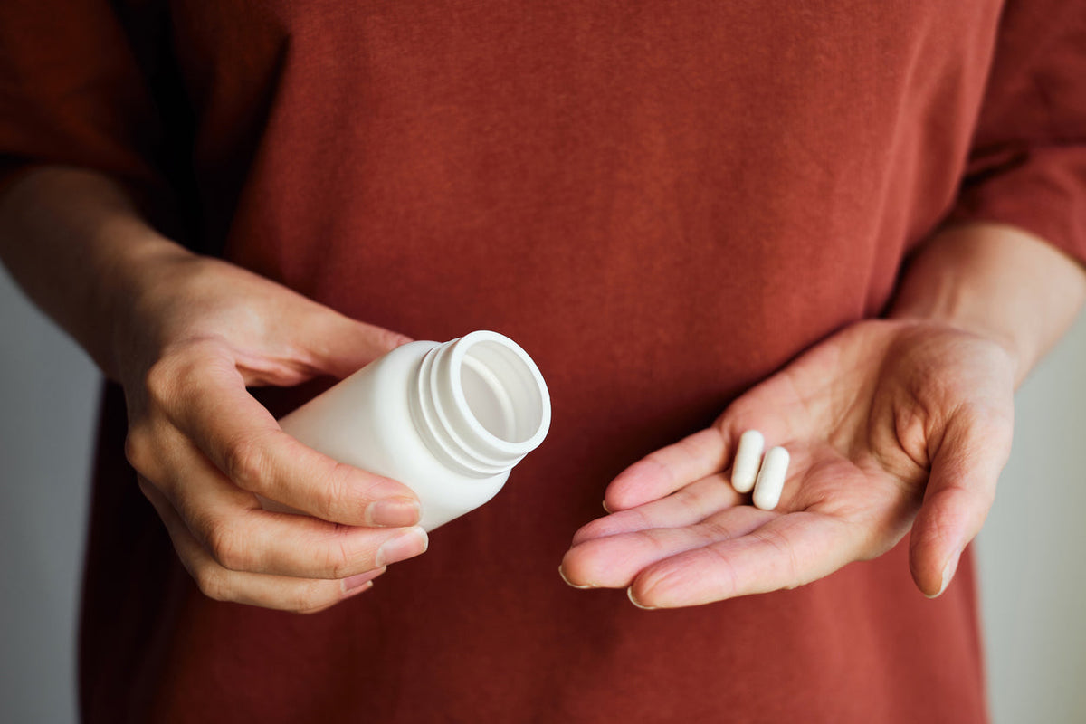 A man holding a supplement container in one hand and two magnesium pills in another