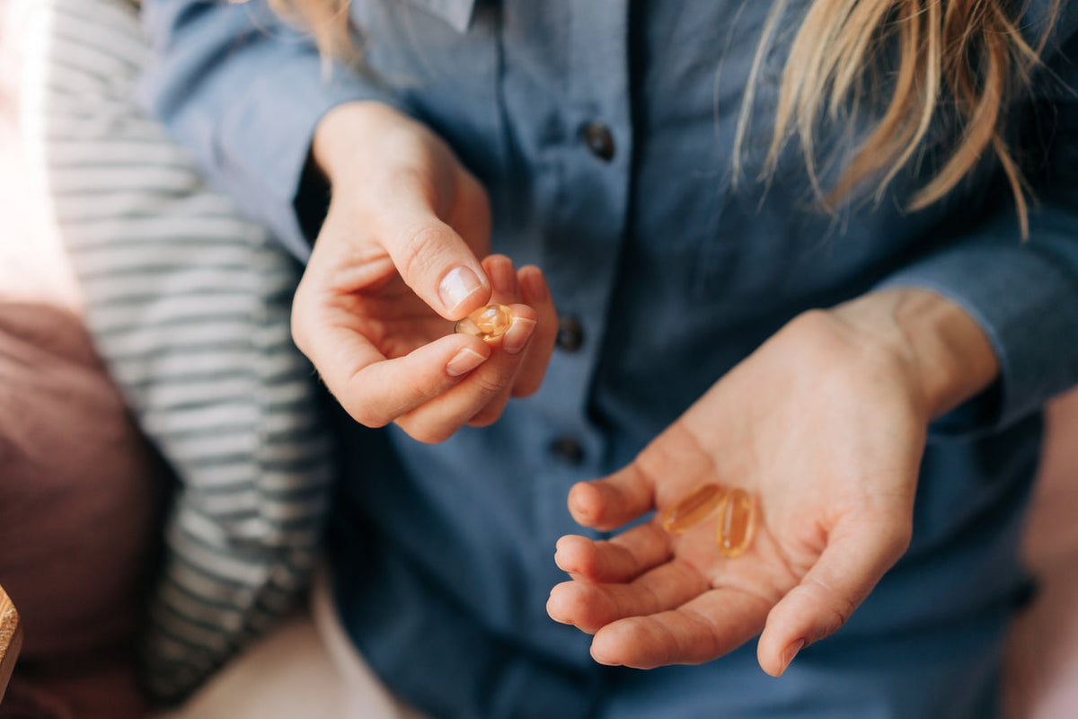 A woman holding two tablets - one Omega 3 and another Vitamin D