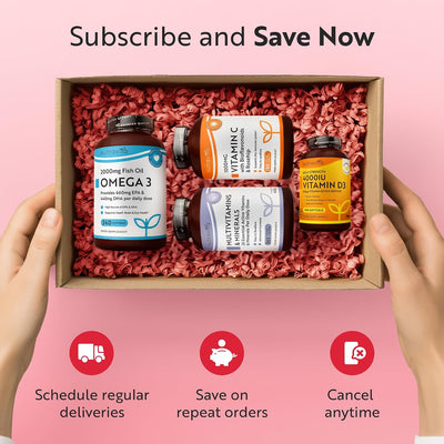 A pair of hands holds a cardboard gift box filled with pink crinkle paper, containing four supplement bottles: Omega 3, Vitamin, Multivitamins, and Vitamin D. The background is pink with text reading 'Subscribe and Save Now' and three feature icons below.